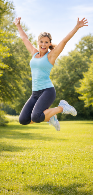 Sportliche Frau springt im Park als Symbol für Fitness und Beweglichkeit